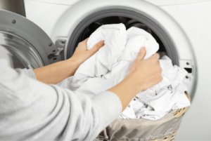 Person in gray sweater places laundry into the washer machine